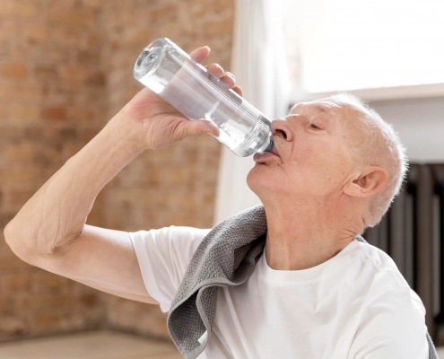 Senior buvant un verre d’eau à domicile pour prévenir la déshydratation