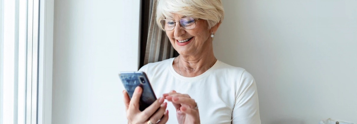 Une personne senior ou un aidant consultant une annonce sur smartphone ou ordinateur avec une attitude attentive, dans une ambiance claire et rassurante.