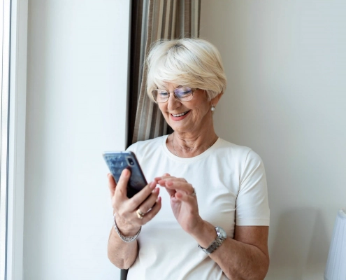 Une personne senior ou un aidant consultant une annonce sur smartphone ou ordinateur avec une attitude attentive, dans une ambiance claire et rassurante.