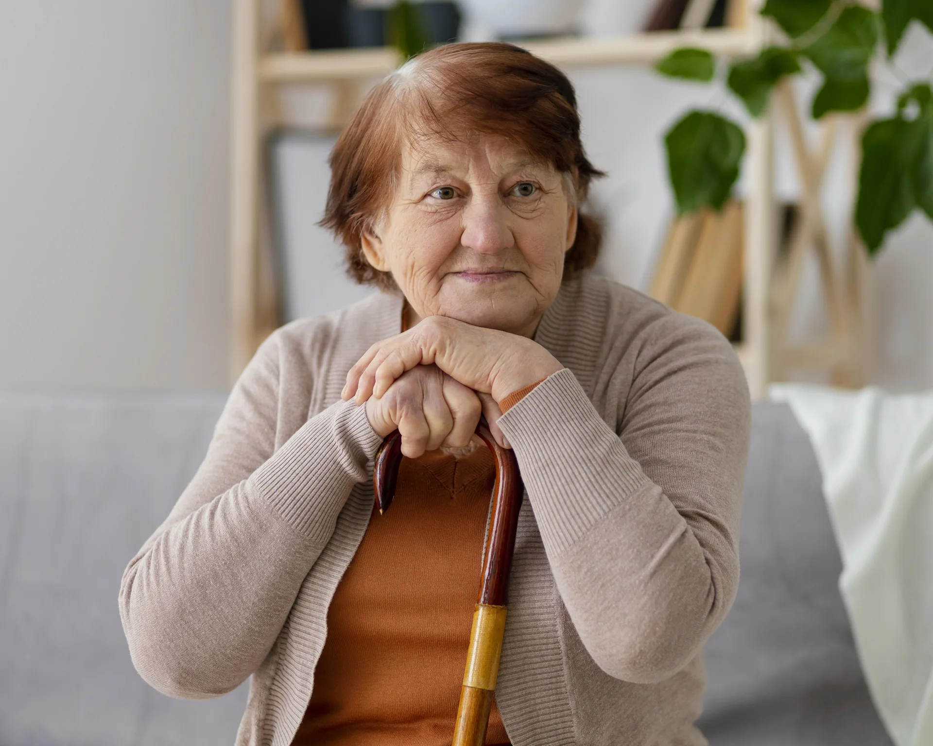 Une femme senior assise chez elle, les mains posées sur sa canne.